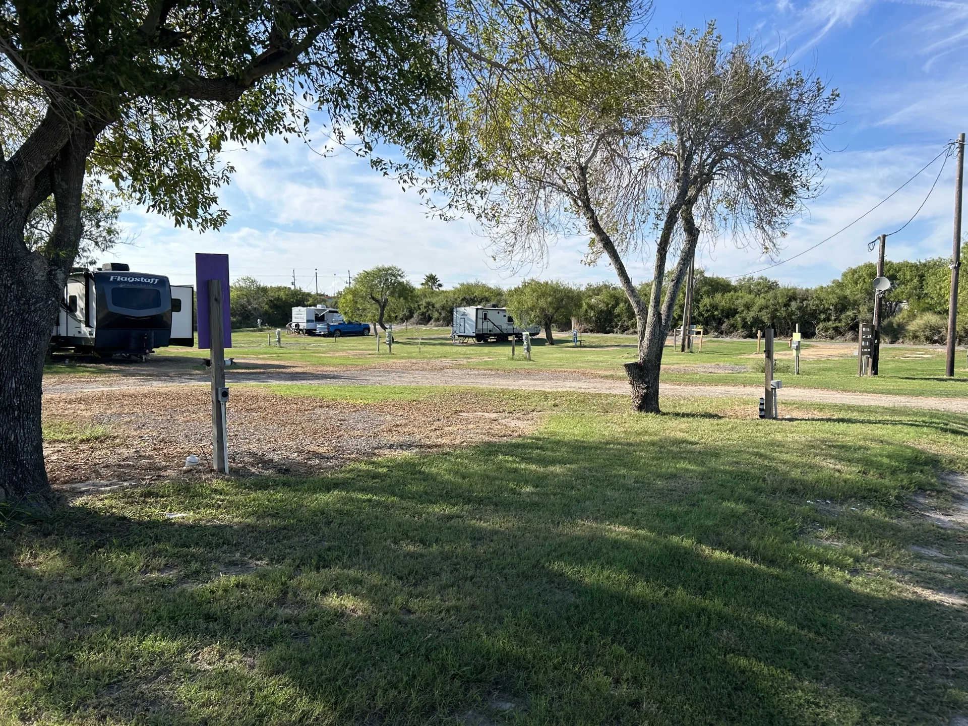 Shaded RV sites with full-hookup pedestals and guest RVs at Down By The Bay RV Resort