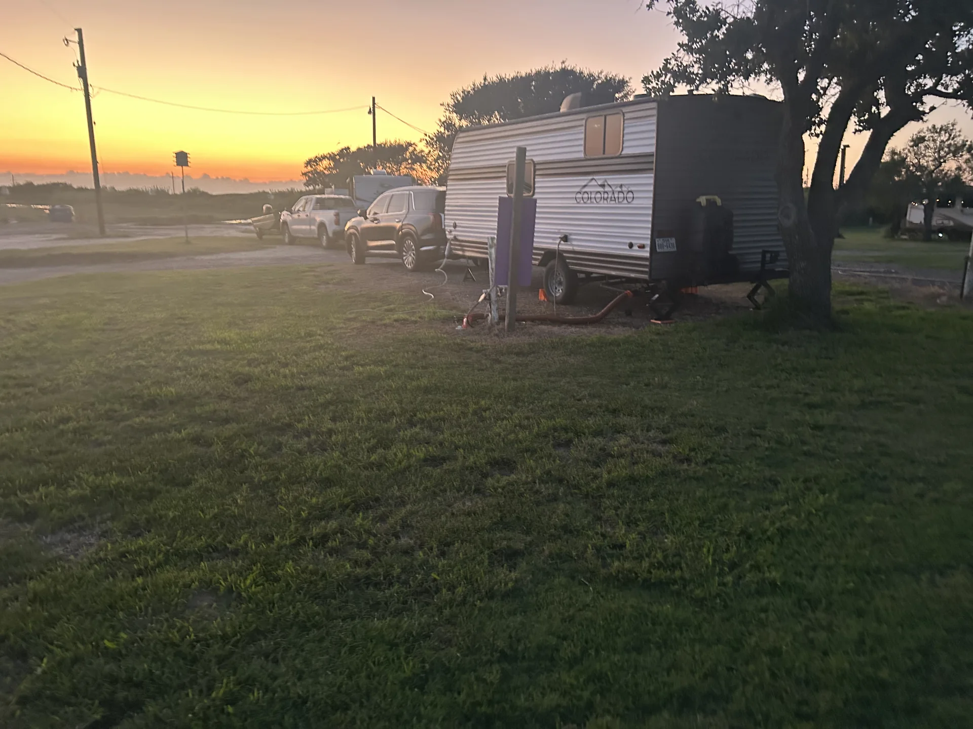 RV site at sunset with green lawn and mature trees at Down By The Bay RV Resort